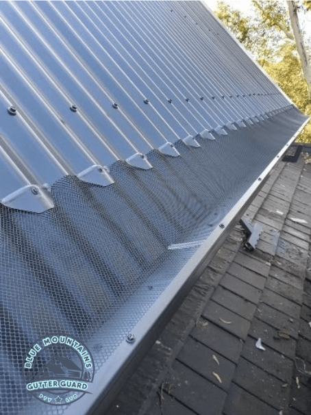 A close-up view of a gutter guard installed on a corrugated roof, showcasing its effectiveness in preventing debris buildup.